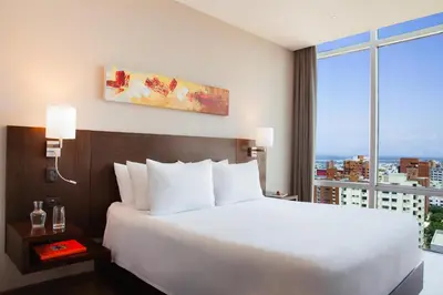 a bedroom with a white bed and a large window at NH Collection Royal Smartsuites in Barranquilla