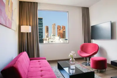 a living room with a pink couch and a red chair at NH Collection Royal Smartsuites in Barranquilla