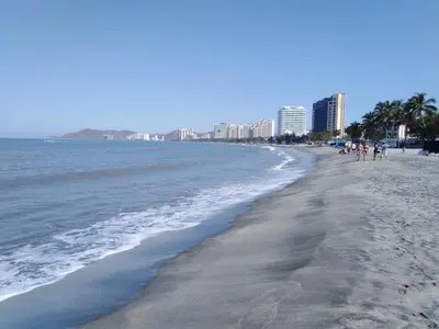 a beach with people walking on the sand and the water at Hotel West Plaza in Santa Marta
