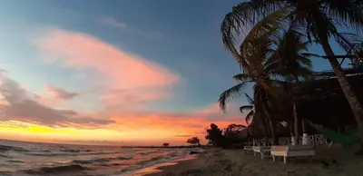 a sunset on a beach with palm trees and the ocean at Mar Amar Casa de Playa in Coveñas