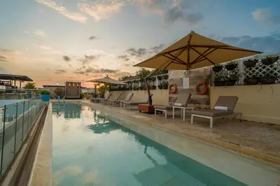 a swimming pool with lounge chairs and an umbrella at Nacar Hotel Cartagena, Curio Collection by Hilton in Cartagena de Indias