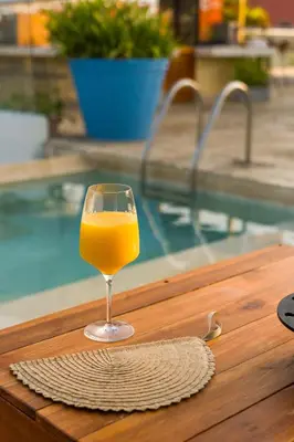 a glass of orange juice sitting on a table next to a pool at Nacar Hotel Cartagena, Curio Collection by Hilton in Cartagena de Indias