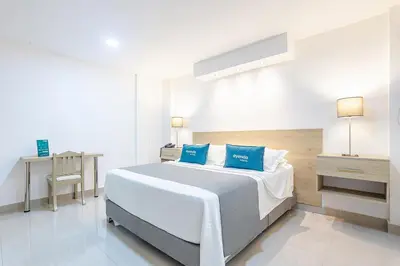 a white bedroom with a large bed with blue pillows at Hotel Ancor in Sincelejo