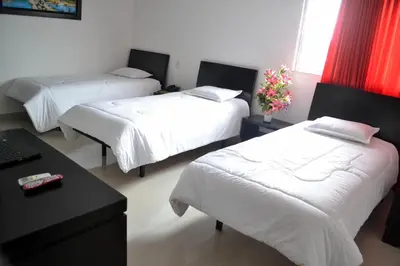 a room with three beds and a desk with a laptop at Hotel Continental Express in Barranquilla