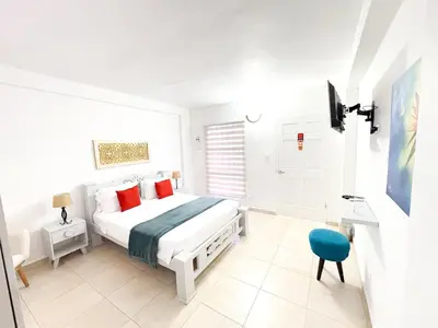 a white bedroom with a bed and a blue chair at Hotel AT THE PARK in Cartagena de Indias