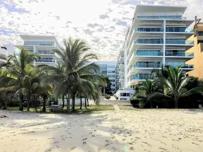 a beach with palm trees in front of a building at Amplio apt de 3 alcobas edificio primera linea de playa in Cartagena de Indias