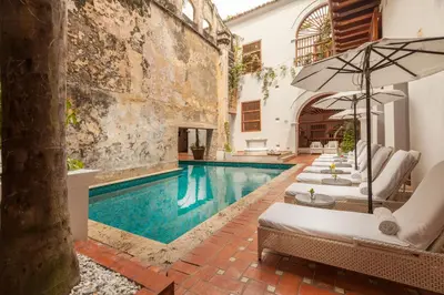 an outdoor pool with lounge chairs and an umbrella at Hotel Casa San Agustin in Cartagena de Indias
