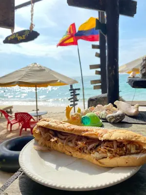 a sandwich on a plate on a table at the beach at Tipiland baru la casa del mono in Playa Blanca