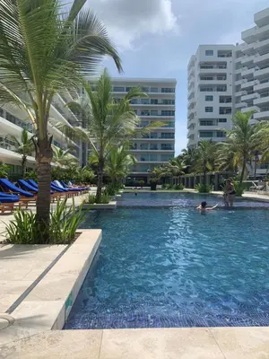 a man in a swimming pool with palm trees and buildings at Apartamento Confort Frente a la Playa en Cartagena! in Cartagena de Indias