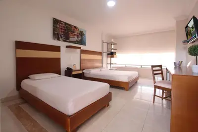 a hotel room with two beds and a table and chair at Hotel Genova Centro in Barranquilla