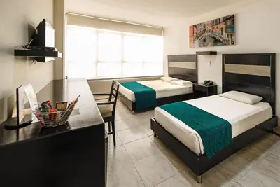 a hotel room with two beds and a desk at Hotel Genova Centro in Barranquilla