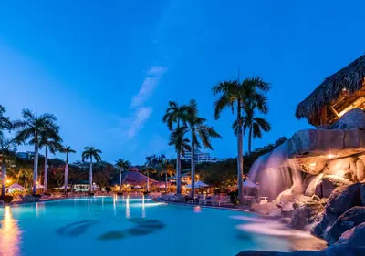 a pool with a waterfall and palm trees at night at Hotel Irotama XXI in Santa Marta