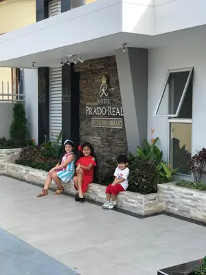 three children sitting on a curb in front of a hotel at Hotel Prado Real in Barranquilla