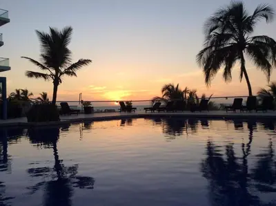 a pool with palm trees in front of a sunset at Apartamento en Cartagena primera linea de Playa Morros Epic in Cartagena de Indias