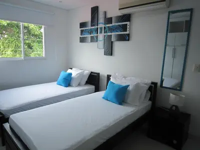 two beds in a white room with blue pillows at Hotel Valmar in Cartagena de Indias