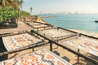 a row of beds on the beach with the city in the background at Éteka Slow Beach Hotel Adults Only in Cartagena de Indias
