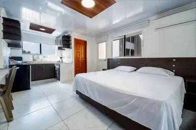 a bedroom with a large white bed and a kitchen at Villa Santos Apartaestudios in Barranquilla