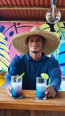 a man wearing a straw hat sitting at a table with two drinks at Anuk Glamping in San Bernardo del Viento