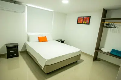 a white bedroom with a bed with an orange pillow at Hotel ITACO in Cartagena de Indias