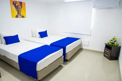 two beds in a white room with blue sheets at Hotel ITACO in Cartagena de Indias