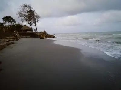 a black beach with a house and the ocean at Palmar del viento cabaña frente al mar in Moñitos