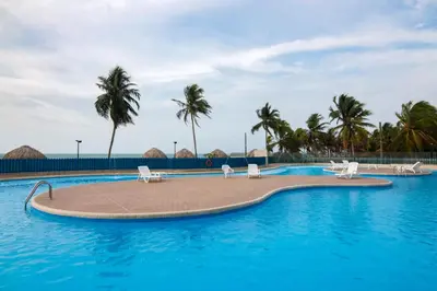 a swimming pool with chairs and palm trees at Hermoso Apartamento Frente al Mar 2 Habitaciones PAZ122 in Coveñitas