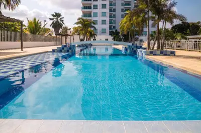 a large blue swimming pool with palm trees and a tall building at Magico Apartamento Frente al Mar 3 Habitaciones AR33 in Coveñas