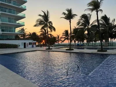 a swimming pool with palm trees and a building at Edificio frente al mar con playas tranquilas in Cartagena de Indias