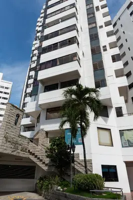 a tall white building with a palm tree in front of it at Apartamento en Bocagrande - Piscina, Jacuzzi y Mar in Cartagena de Indias