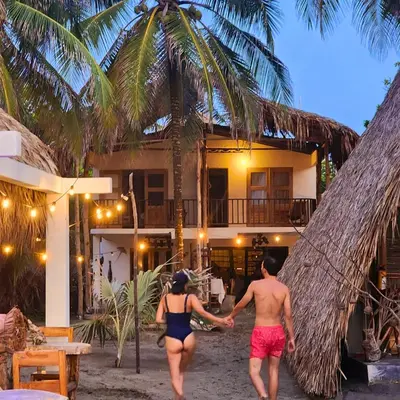a man and woman walking towards a house on the beach at älanacasadeplaya in San Bernardo del Viento