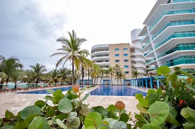 a resort swimming pool with palm trees and a building at Cartagena primera línea de playa azul frente al mar in Cartagena de Indias