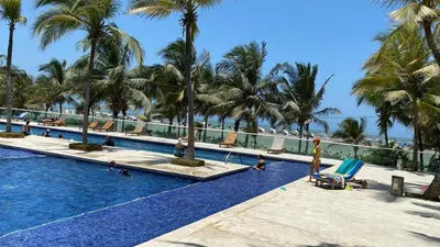 a resort swimming pool with palm trees and a beach at Cartagena primera línea de playa azul frente al mar in Cartagena de Indias