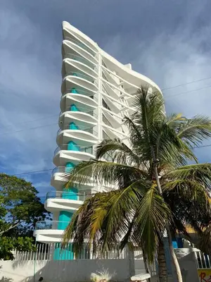 a tall white building with a palm tree in front of it at Magico Apartamento Frente al Mar 3 Habitaciones FB73 in Coveñas