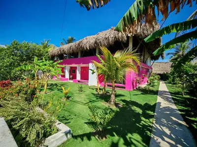 a pink house with a thatched roof at Tata Lolo in Coveñas
