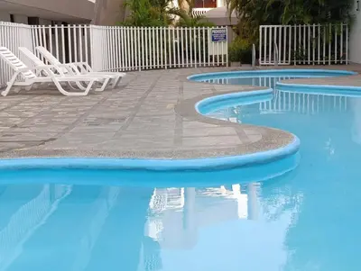 a swimming pool with two white chairs and blue water at Amplio dúplex con playa y mall a una cuadra in Santa Marta
