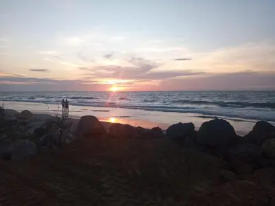 a sunset over the ocean with rocks on the beach at Cabaña frente al mar Encanto del Viento in San Bernardo del Viento