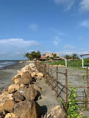 a fence on a beach with rocks and the ocean at Cabaña frente al mar Encanto del Viento in San Bernardo del Viento