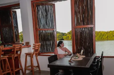 a woman sitting at a table with a view of a river at Hostal Casa en la Ciénaga Rincon del Mar in Rincón
