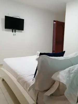 a bed with white sheets and a tv on the wall at CC House Cartagena in Cartagena de Indias