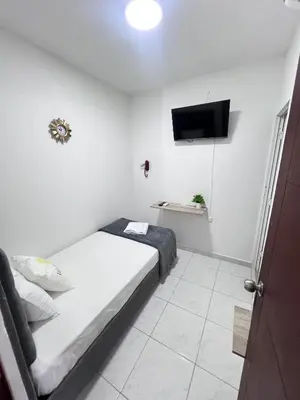 a small white bedroom with a bed and a flat screen tv at Garden Home Hostal in Barranquilla