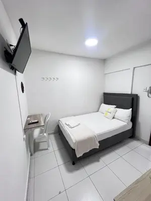 a small white room with a bed and a desk at Garden Home Hostal in Barranquilla