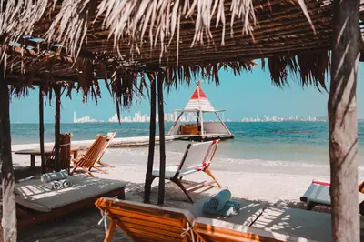 a beach with chairs and a straw umbrella and the ocean at Fenix Beach Cartagena in Tierra Bomba