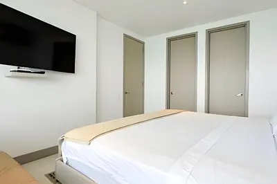 a white bedroom with a bed and a flat screen tv at Laurdhomes Lujoso Apto Piso 28 frente al mar, 2BTH in Cartagena de Indias