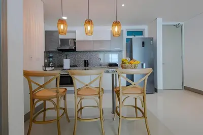 a kitchen with three bar stools and a refrigerator at Laurdhomes Lujoso Apto Piso 28 frente al mar, 2BTH in Cartagena de Indias