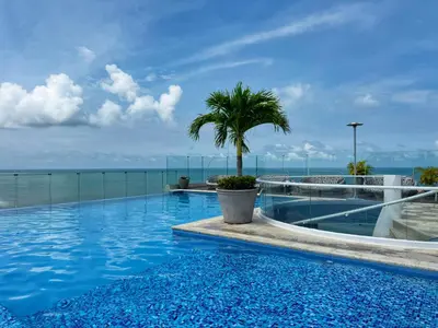 a swimming pool with a palm tree and the ocean at ¡Amazing Beach Dúplex! Infinity Pool / Rooftop in Cartagena de Indias