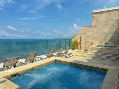 a swimming pool with chairs and the ocean in the background at ¡Amazing Beach Dúplex! Infinity Pool / Rooftop in Cartagena de Indias
