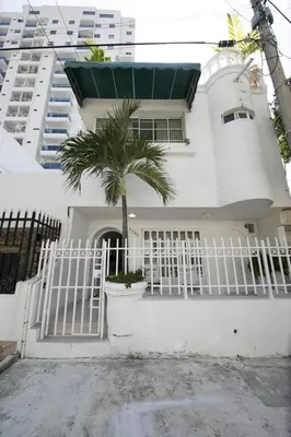 a white house with a white gate and a palm tree at Hostal Casa Dandy in Cartagena de Indias