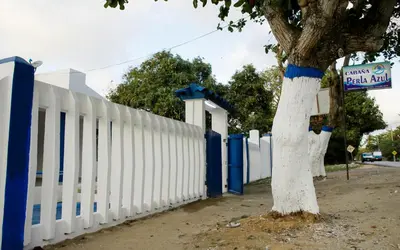 a white fence with a tree next to it at Cabaña Perla Azul in Coveñas