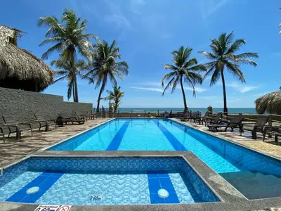 a swimming pool with palm trees and the ocean at Apto 1er piso frente a la playa y con piscina in San Bernardo del Viento